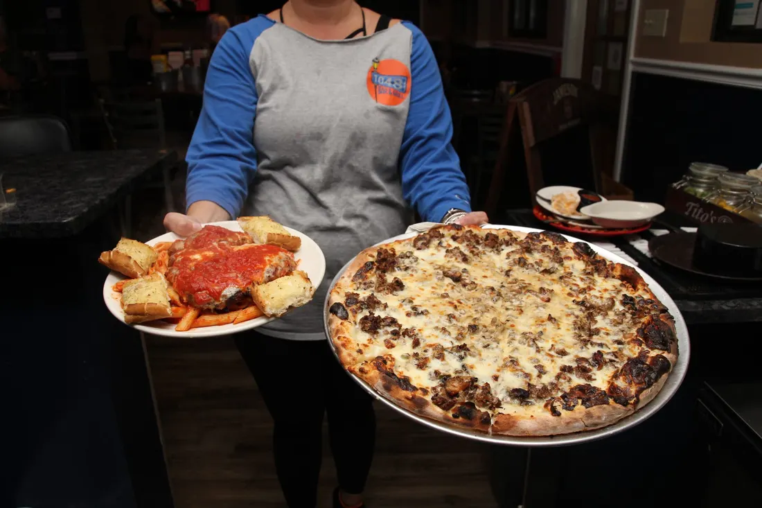 A server carrying a pizza and a plate of food